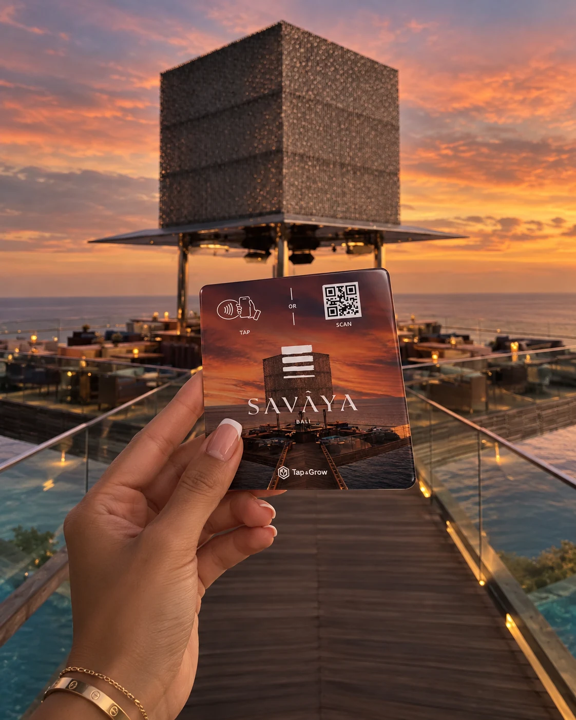 Illustrative SAVAYA branded Tap & Grow NFC card held in front of the Cube at sunset